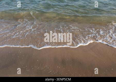 Una vista ad alto angolo delle dolci onde oceaniche che si innalzano su una spiaggia sabbiosa, creando dettagliati motivi di schiuma marina bianca nel Mare interno, Qatar. Foto Stock