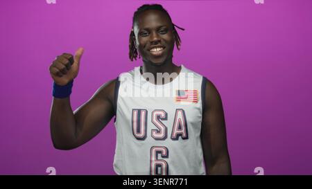 La maglia da basket Man in usa mostra i pollici e la mano alzata in studio con sfondo magenta; celebrazione della fiducia. Foto Stock