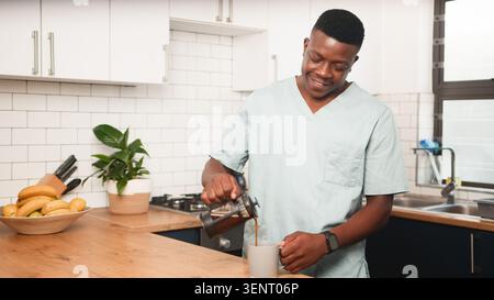 Operatore sanitario versare caffè in cucina durante la routine mattutina rilassata a casa Foto Stock