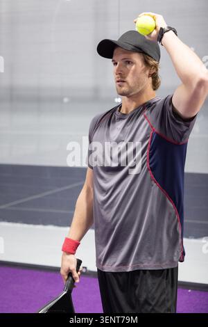 Atleta maschile che serve, tiene la palla gialla e la pagaia, indossa un cappello nero sul campo viola Foto Stock