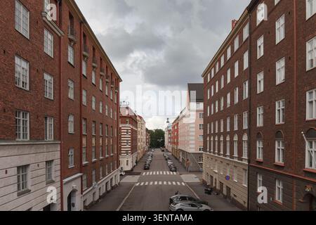 HELSINKI, FINLANDIA - 11 AGOSTO 2025: Strada urbana simmetrica con alti edifici in mattoni rossi e veicoli parcheggiati sotto il cielo nuvoloso. Foto Stock