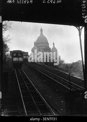 La funicolare di Montmartre opera sotto il Sacré-Coeur a Parigi in una fotografia del 1927 commissionata da Agence Meurisse. La vista monocromatica registra il trasporto urbano accanto a uno dei principali luoghi di interesse religioso della città durante gli anni tra le due guerre. Foto Stock