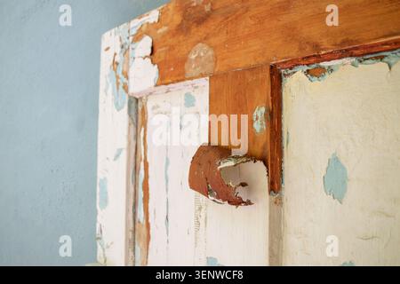 Vista di una vecchia portiera bianca sporca con vernice sbucciante. Uno strato di vernice vecchia rotolata in un rotolo con una spatola sulla porta. Rimozione Foto Stock