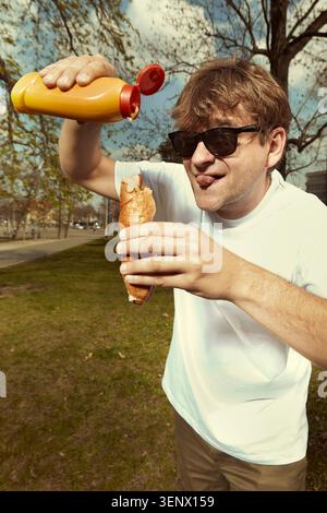 Uomo in strada che mangia hot dog con senape, ketchup e panino Foto Stock