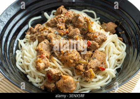 Primo piano di saporiti spaghetti di manzo coreano con semi di sesamo in un recipiente di ceramica nera Foto Stock