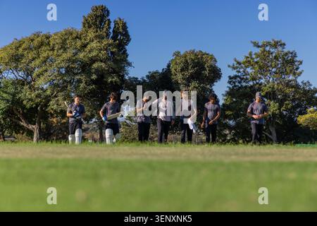 Diversi compagni di squadra maschi di cricket che camminano su un campo sportivo erboso portando pipistrelli, piazzole e cappellini Foto Stock