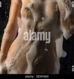 Una donna sta dietro un vetro appannato, circondato da bolle, godendosi un bagno rilassante, creando un'atmosfera serena e tranquilla Foto Stock