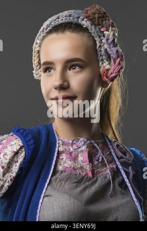 Una giovane donna sfoggia un abito tradizionale con fascia intrecciata, sorridendo dolcemente mentre i suoi capelli cadono elegantemente dietro di lei Foto Stock