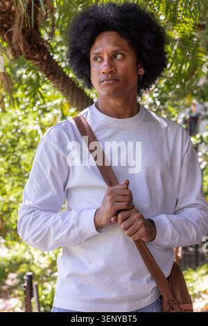Uomo afro-americano che regge il cinturino con indosso una camicia bianca a maniche lunghe sotto gli alberi illuminati dal sole Foto Stock