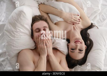 Una donna e un uomo condividono un momento giocoso a letto, mostrando il loro legame e la loro gioia mentre si coccolano sotto coperte morbide Foto Stock