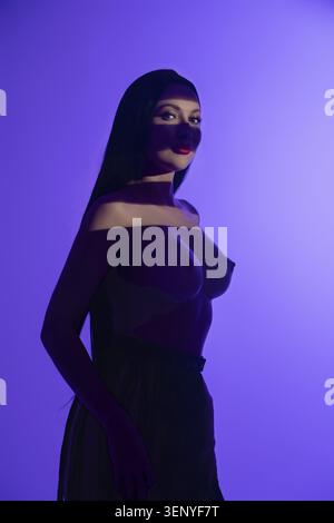 Una donna si trova elegantemente sotto una cascata di luci colorate per mostrare la sua bellezza e sicurezza. Le tonalità vivaci creano contrasti sorprendenti Foto Stock
