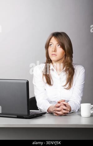 Una donna d'affari è seduta in ufficio con un computer portatile e guarda con attenzione lateralmente Foto Stock