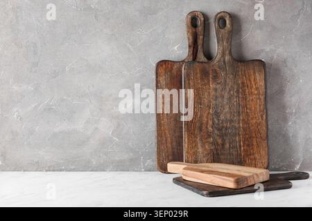 Taglieri in legno rustico e utensili da cucina su ripiano in marmo bianco con sfondo in cemento grigio, lo sfondo presenta un Foto Stock