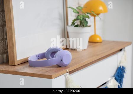 Moderne cuffie senza fili lavanda su un tavolo in legno con pianta e lampada, tecnologia per l'ufficio e relax Foto Stock