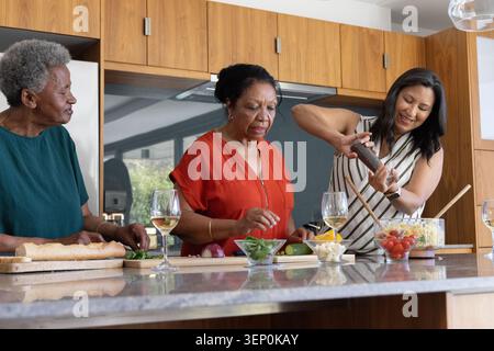 Famiglia afroamericana multigenerazionale che affetta baguette e insalata di salviette all'isola di Kitchen Foto Stock