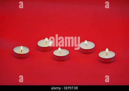 Cinque piccole candele rotonde bruciate su sfondo rosso brillante. Foto di alta qualità Foto Stock