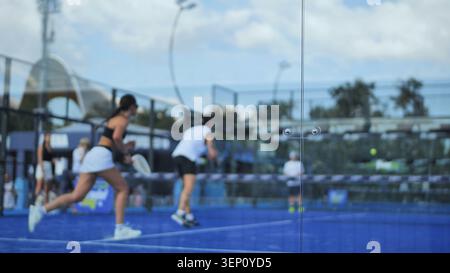 I giocatori di Padel gareggiano sul campo blu, impegnandosi in intense azioni e partite sportive Foto Stock
