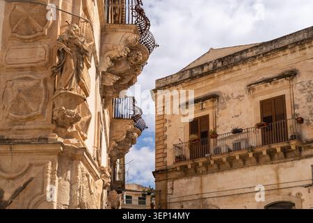 Statue in pietra ornate e balconi in ferro battuto su edifici barocchi storici a Scicli in Sicilia Foto Stock