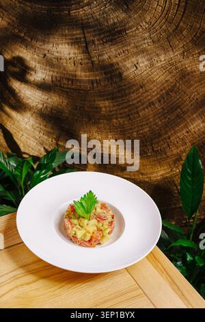 Tartare di salmone gourmet con avocado su fondo in legno. Il piatto è composto da frutti di mare e guarnigioni tritati finemente. Foto Stock