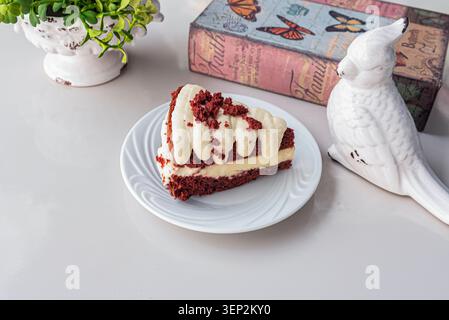 Allestimento minimalista con fetta di torta di velluto rosso. Metti a fuoco luci soffuse, texture cremose e accenti rossi. Ideale per pasticceria, forno Foto Stock