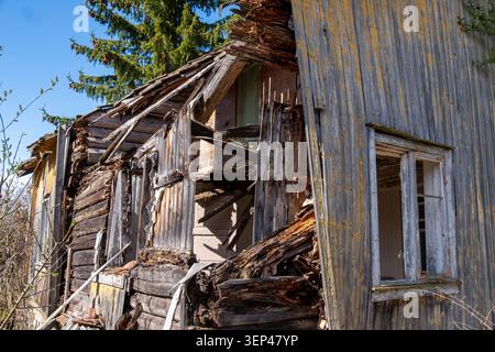 Casa in legno abbandonata gravemente deteriorata con pareti crollate e struttura interna esposta che mostra decadimento avanzato e negligenza Foto Stock