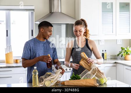 Coppia che si disimballa in cucina portando sacchetti in rete per preparare pane e verdure con contrassegni di movimento Foto Stock