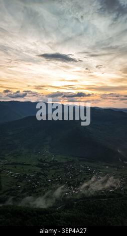 I ripidi pendii boscosi incorniciano una lunga valle piena di nebbia crescente. Dall'alto, il drone rivela strade tortuose, villaggi e fiumi che si intrecciano Foto Stock