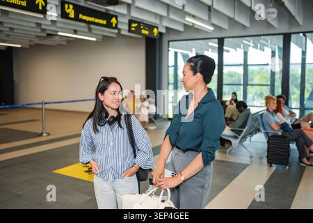 Due persone in piedi in un corridoio dell'aeroporto con bagagli e passeggeri sullo sfondo Foto Stock