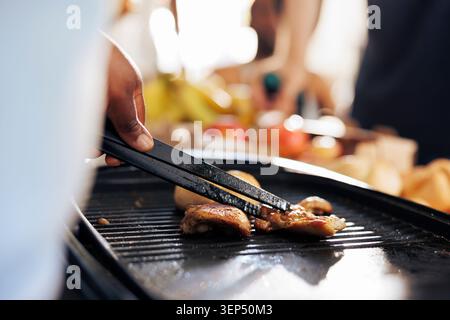 L'individuo afroamericano prepara pasti sulla griglia evidenziando gli sforzi umanitari per alleviare la fame e la povertà. Lo scatto dettagliato cattura un atto caritatevole di cucina per i meno fortunati. Foto Stock
