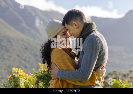 Coppia romantica che abbraccia la fronte pressata nella valle del sole indossando berretto senape e maglie grigie Foto Stock