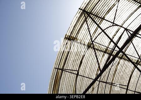 Una composizione minimalista caratterizzata da una struttura ricurva del tetto ondulata contro un cielo azzurro. Evidenziando texture ritmiche, cornici geometriche in metallo, Foto Stock