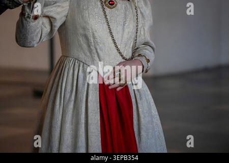 Un primo piano di uno storico abito in broccato bianco con un inserto rosso, anelli d'oro ornati e una catena pendente che trasmette stile aristocratico, costume d'epoca Foto Stock