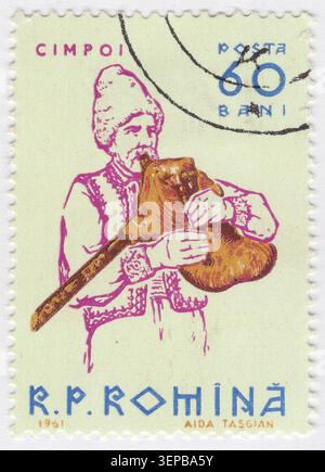 ROMANIA - 1961 settembre 20: 60 Ban francobollo multicolore raffigurante opere d'arte contadina che suona Cimpoi celebra il ricco patrimonio musicale rumeno mettendo in risalto uno strumento popolare rumeno tradizionale. Un vecchio musicista maschile che indossa un tradizionale vestiario ricamato e un cappello di alta pelliccia mentre suona una cornamusa nativa. Tiene il chanter e stringe la borsa di pelle con le mani per eseguire melodie storiche del folklore. Questa opera d'arte enfatizza l'identità nazionale, l'arte contadina e le tradizioni culturali etniche all'interno del programma artistico sostenuto dallo stato della Repubblica Popolare Romena Foto Stock