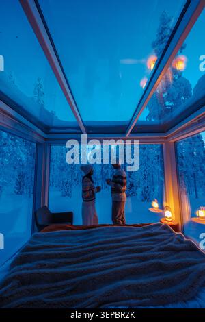 Due persone si godono un momento sereno in una cabina di vetro, circondata da paesaggi innevati sotto uno splendido cielo blu ad Akaslompolo, Lapponia, Finlandia. Una fuga invernale ideale. Foto Stock