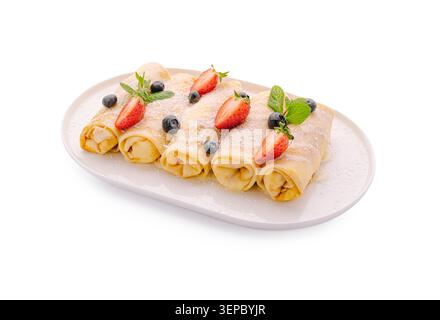 Le crepes sono ripiene di panna dolce e frutta. Fragole fresche, mirtilli e foglie di menta sono sopra. Questo piatto è servito su un piatto bianco, ideale per colazione o dessert. Foto Stock