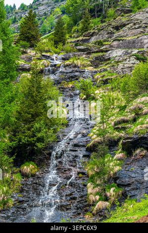 Fotografia verticale di una piccola cascata alpina a Pfelders, alto Adige, Italia. L'acqua scorre e si tuffa giù da rocce umide scure su una ripida montagna Foto Stock