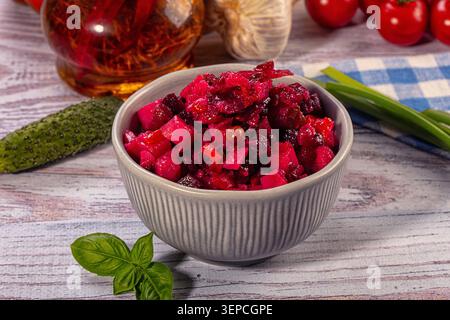 Insalata tradizionale di barbabietole con verdure a dadini in ciotola grigia su fondo rustico in legno. Vivace piatto magenta circondato da aglio fresco, sottaceti, lei Foto Stock