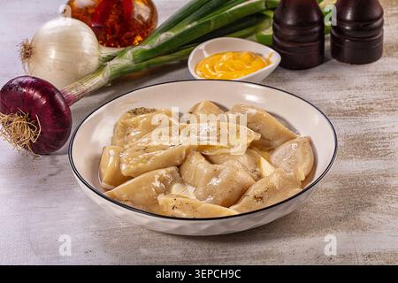 Deliziosi gnocchi fatti in casa ripieni di formaggio di patate, conditi con burro fuso e cipolle fritte croccanti. Servito in un recipiente di ceramica bianco con bordo nero Foto Stock