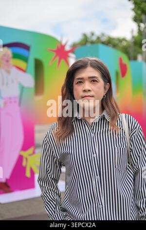 Un ritratto verticale in vita di una donna asiatica transgender di mezza età che guarda la fotocamera contro un dorso sfocato e colorato Foto Stock
