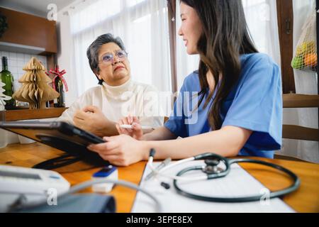 Grave donna asiatica senior sta ascoltando infermiera spiegare come utilizzare la tecnologia tablet in consultazione con i dispositivi medici in primo piano. discutere di guarigione Foto Stock
