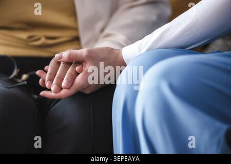 Avvicinare le mani dell'infermiere appoggiate delicatamente su ciascun supporto paziente senior seduto fianco a fianco, operatore sanitario con focus selettivo che conforta la donna anziana che tocca l'incoraggiamento Foto Stock