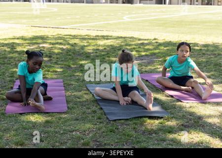 Diverse bambine che indossano camicie color verde acqua sedute su tappetini da ginnastica su un campo erboso con pali d'oro Foto Stock