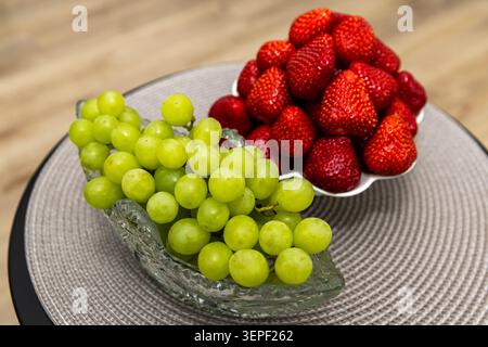Uve verdi fresche e fragole mature esposte in eleganti ciotole, che offrono una sana e colorata selezione di frutta di stagione. Foto Stock