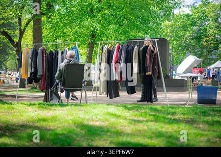 Scaffali di abbigliamento pieni di abbigliamento vintage in un mercato delle pulci all'aperto in un parco soleggiato di Helsinki. Un fornitore siede su una sedia pieghevole in attesa dei clienti Foto Stock