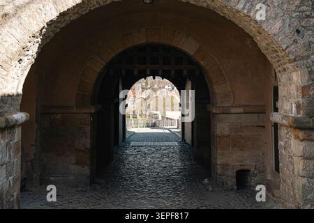 Erfurt, Germania - 27 marzo 2026. Passaggio ad arco in pietra all'interno della Cittadella di Petersberg con marciapiedi in acciottolato, vecchie mura della fortezza, dettagli di cancelli in legno, a. Foto Stock