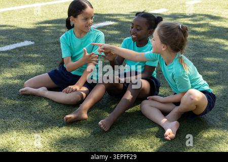 Diverse ragazze in età scolare sedute a piedi nudi sul tappeto erboso con uniformi di color ottanio abbinate, a indicare Foto Stock