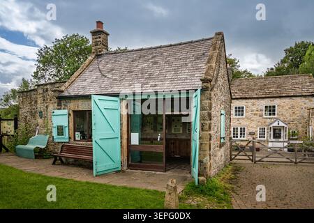 La storica Old Market Hall, costruita in pietra, presenta doppie porte in legno blu pallido sul verde del villaggio di Eyam, Derbyshire Foto Stock
