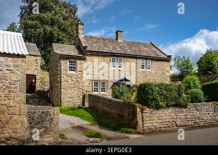 Vista a tre quarti dello storico cottage Laburnum costruito in pietra dietro un tradizionale muro di confine in pietra a secco nel villaggio di Eyam, Derbyshire Foto Stock