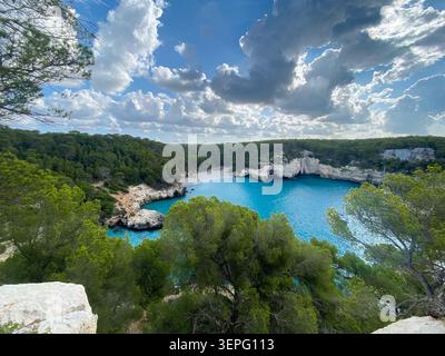 Vista panoramica ad alto angolo della baia di Cala Mitjana a Minorca, Isole Baleari, Spagna. L'immacolata spiaggia di sabbia bianca è circondata da lussureggianti prati di pino Foto Stock