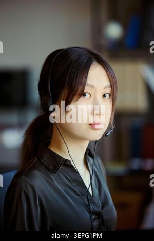 Ritratto di una giovane donna asiatica che indossa le cuffie, lavora in ufficio di contact centre e guarda la fotocamera, rappresentando l'assistenza e l'assistenza clienti. Per CRM, help desk, outsourcing marketing, verticale Foto Stock